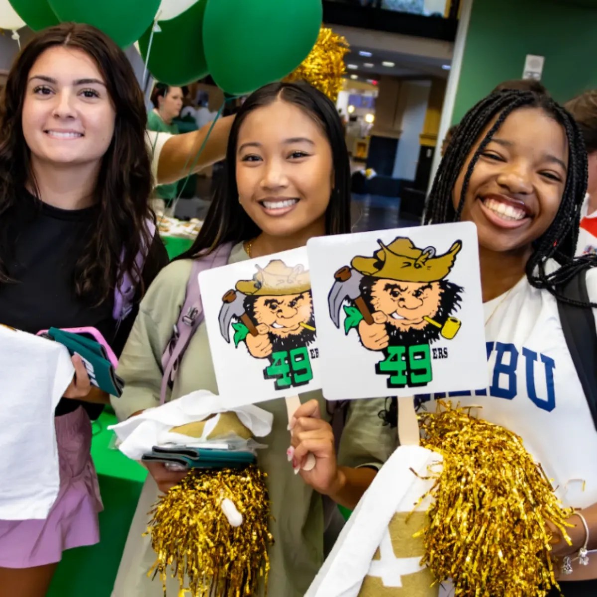 Three smiling female students with Niner swag