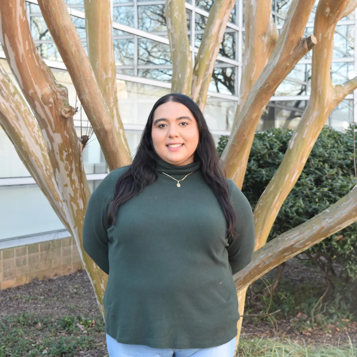person in green turtleneck standing in front of tree smiling