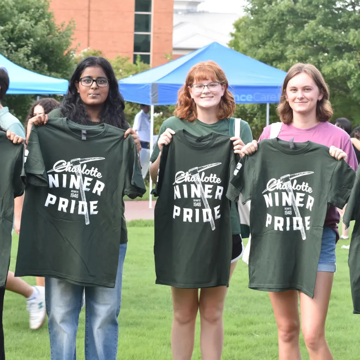 Five students holding up Niner Pride shirts at New Student Welcome